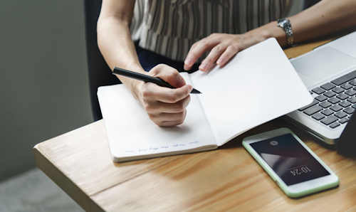 Woman writing in notebook with phone on desk