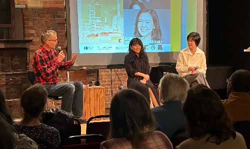 Two women sit on a stage with a man holding a microphone