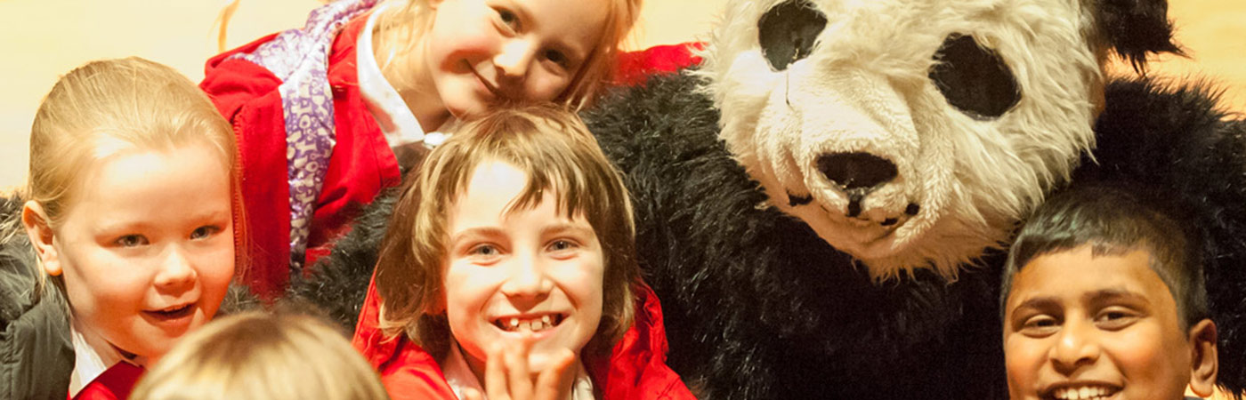 Children in primary school laughing with someone in a panda costume