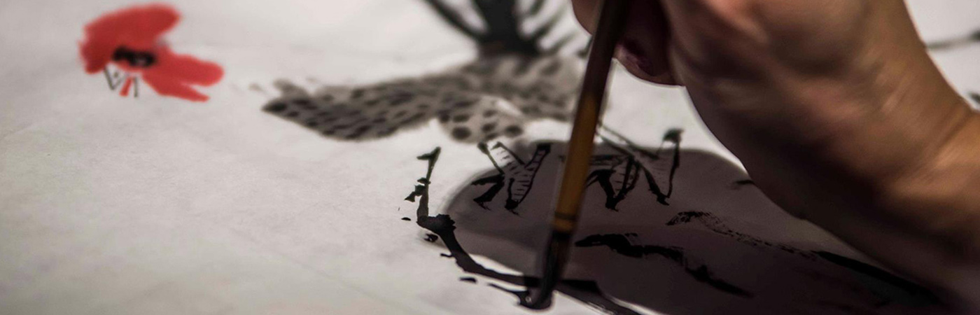 Person writing with a paint brush on paper with black ink