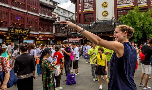 Female student taking a photograph in a busy China street with shops and temples in the background